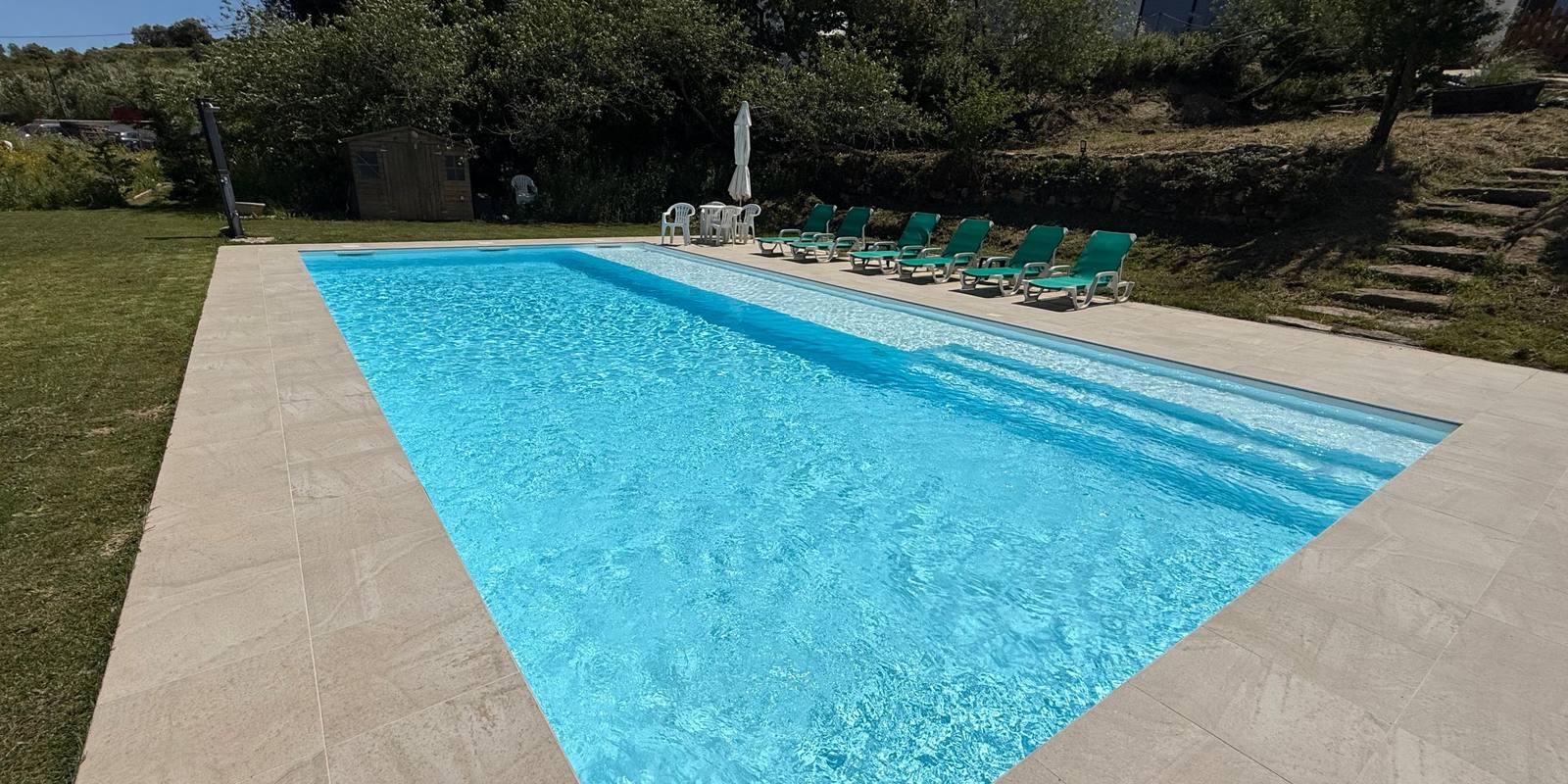The swimming pool on the lawn, with sun loungers and the houses on the slope behind