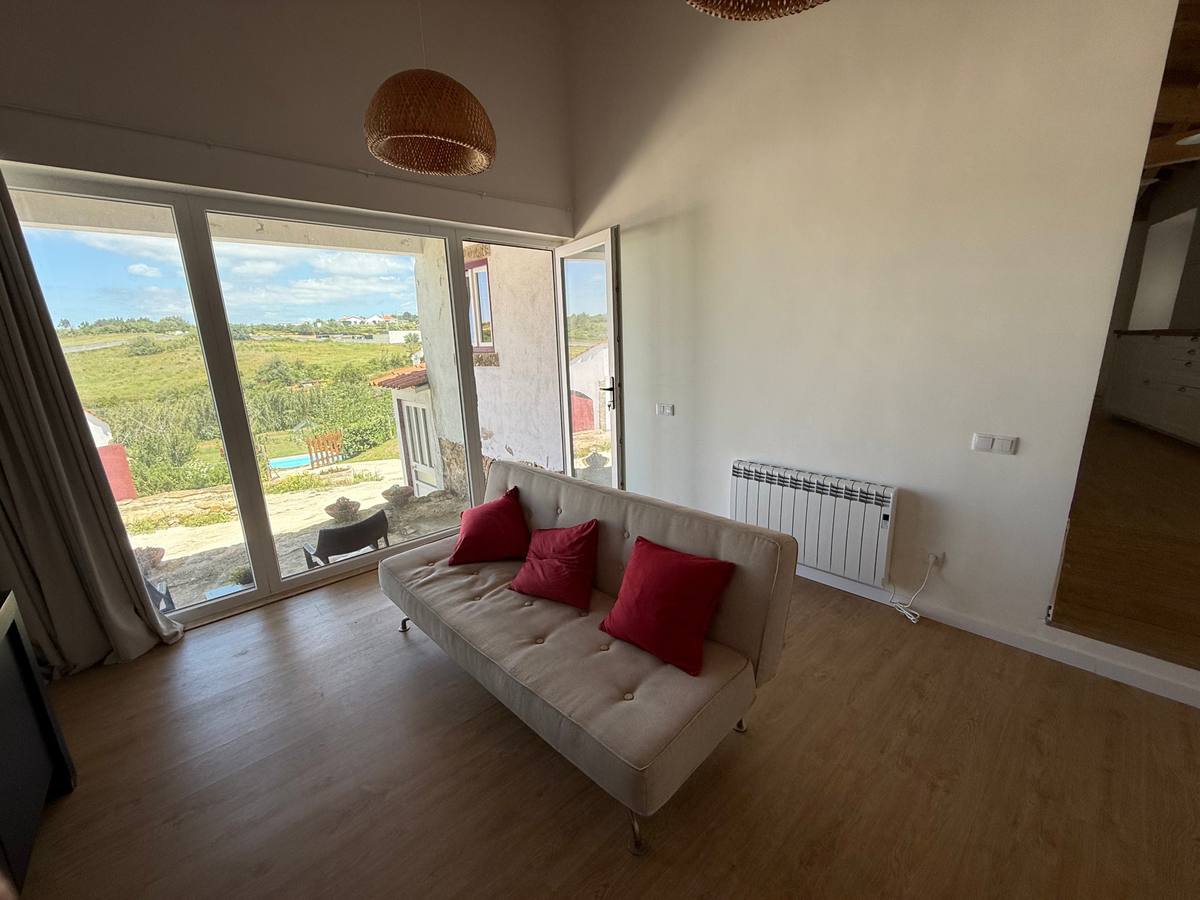 A sofa with red cushions by a wall of windows looking out over the valley